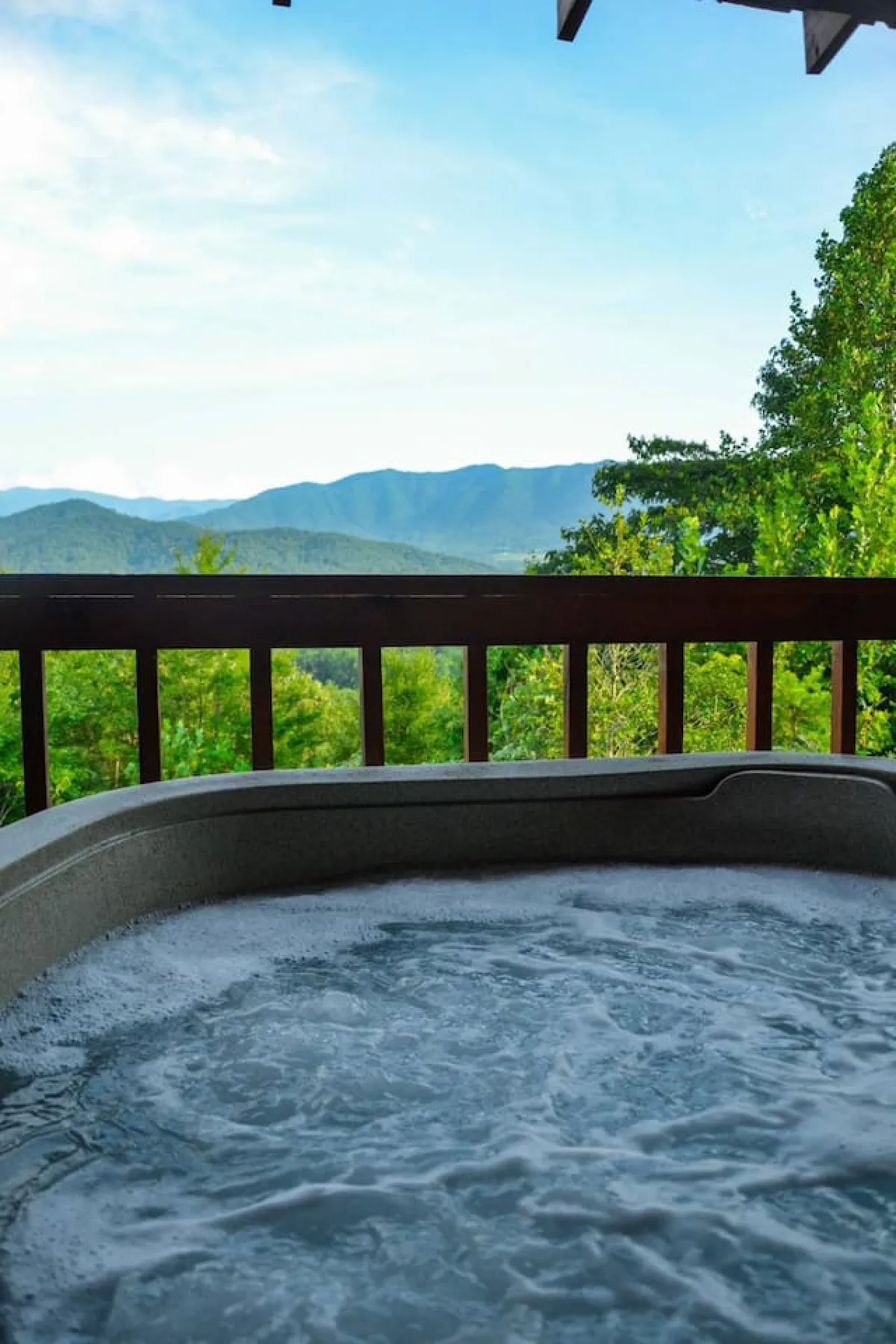 A bubbling hot tub sits on a wooden deck, surrounded by a sturdy railing and overlooking a panoramic mountain view. The inviting water and tranquil setting highlight a key relaxation amenity.
