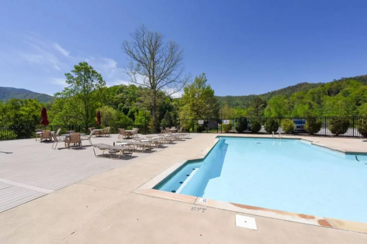 The swimming pool area is bordered by lush greenery, with several lounge chairs set up for sunbathing and socializing. The tranquil setting is perfect for quiet mornings or lively poolside gatherings with friends and family.