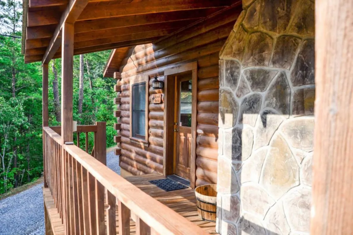 A welcoming log cabin with stone accents and a wooden railing, set amidst a tranquil natural backdrop. The inviting front porch hints at relaxation and the cabin's connection to the outdoors, perfect for travelers with pets.
