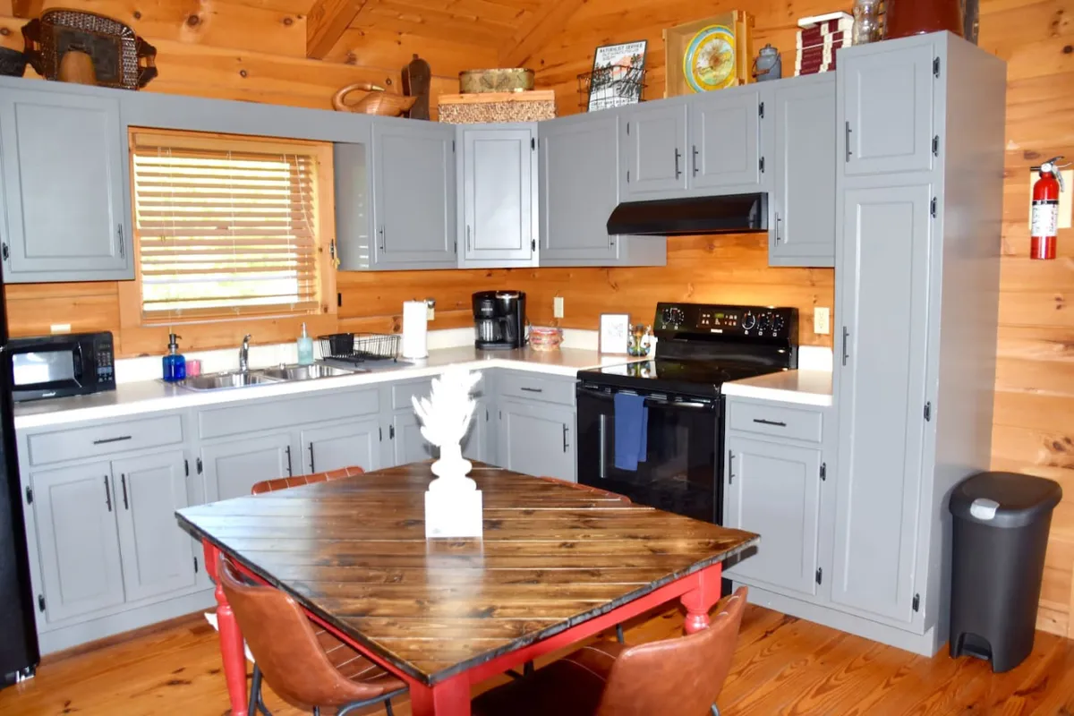 A bright, inviting kitchen and dining space with a central kitchen table surrounded by wooden cabinets, modern appliances, and a window that lets in natural light. The layout encourages family meals, holiday gatherings, and friendly conversation.