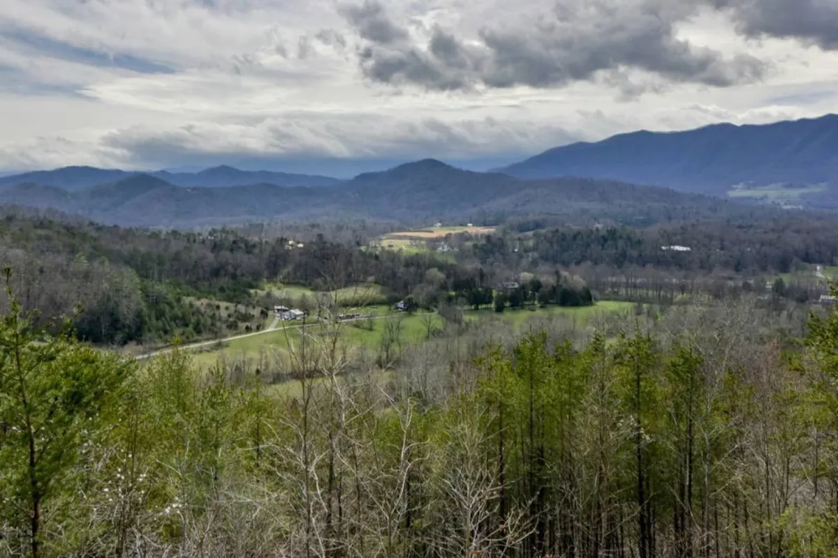 A panoramic view showcasing mountains, a lush valley, winding road, and farmland. Early morning mist hangs over the landscape, evoking a tranquil, immersive natural environment.