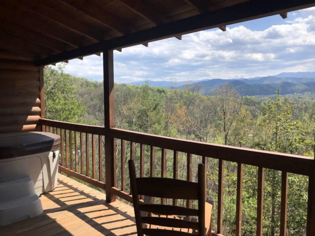 A wooden deck featuring a hot tub, mountain views, and a comfortable chair. The inviting space is perfect for relaxing, reading, or enjoying the surrounding scenery, echoing the property's river access and outdoor adventure opportunities.