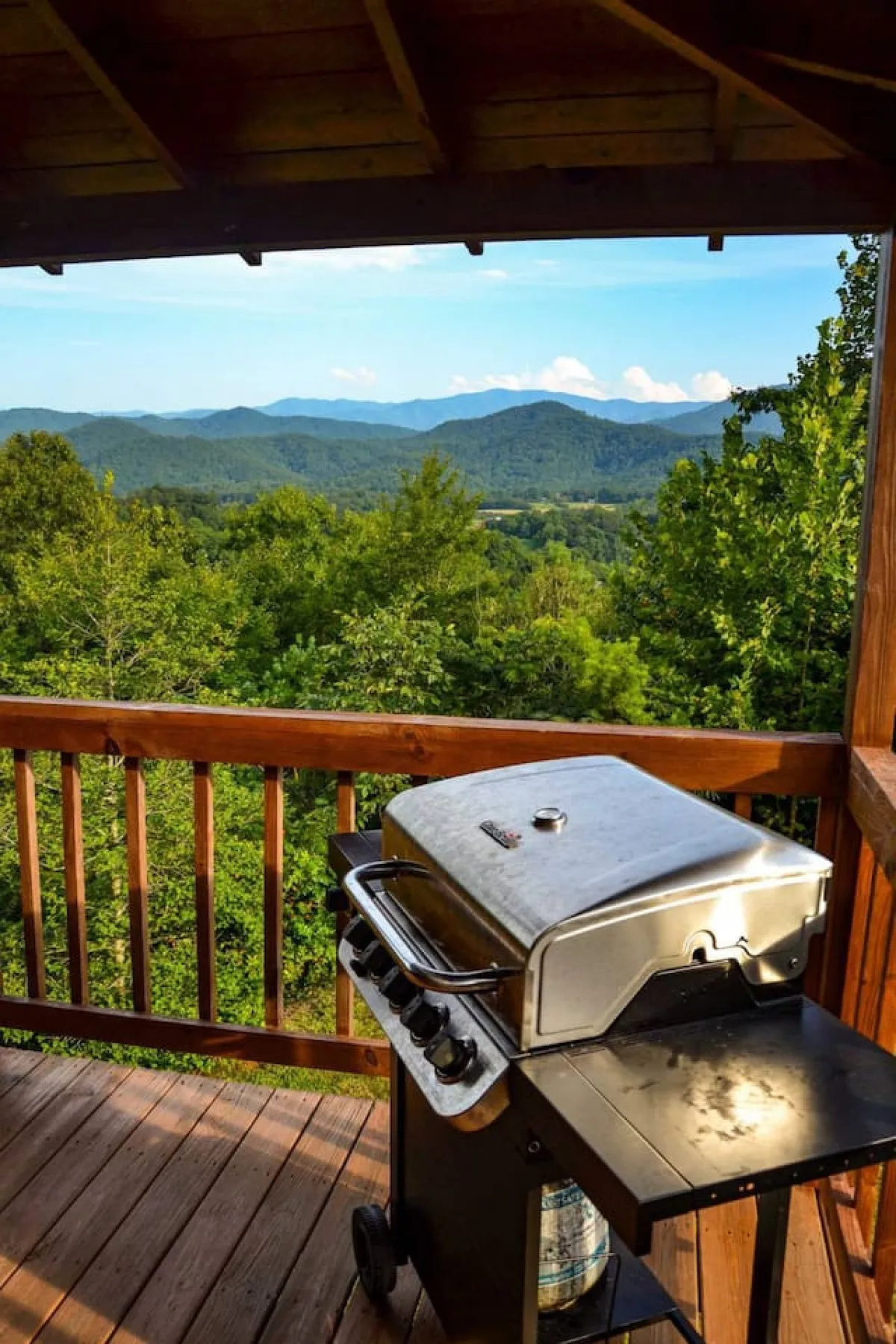 The image features a propane grill on a wooden deck, with the deck railing framing a stunning mountain view in the background. This setup is ideal for al fresco meals and outdoor gatherings, aligning with the deck's entertaining amenities.