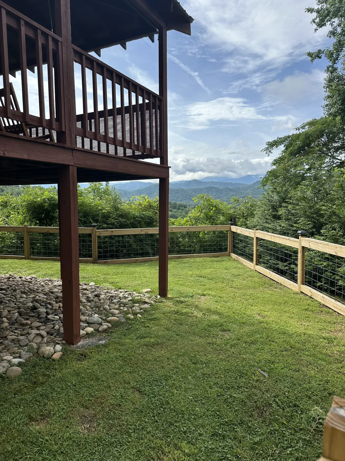 This image captures a wide view of the wooden deck with a sweeping mountain backdrop and grassy area in the foreground. The spaciousness of the deck is evident, and the surrounding nature creates an inviting atmosphere for outdoor relaxation or gatherings.